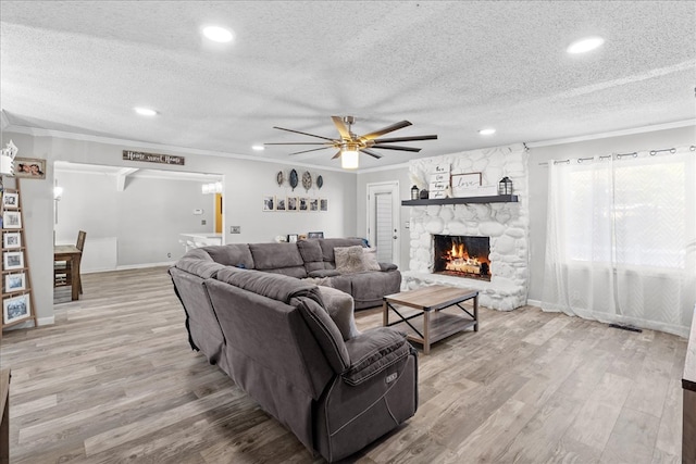 living room featuring ornamental molding, a stone fireplace, a textured ceiling, and light wood-type flooring