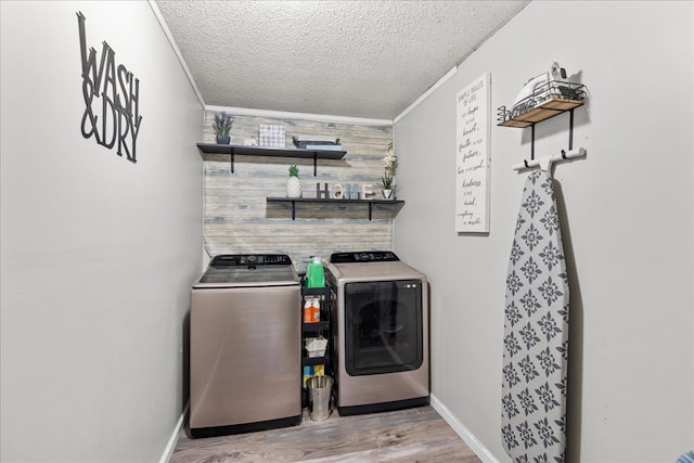 laundry room with wood walls, a textured ceiling, light hardwood / wood-style flooring, ornamental molding, and washer and clothes dryer