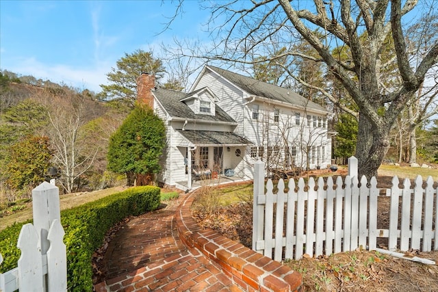 view of front of home featuring roof with shingles, covered porch, a fenced front yard, and a chimney