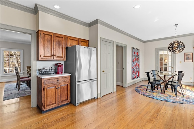 kitchen with brown cabinetry, freestanding refrigerator, light countertops, light wood-style floors, and crown molding