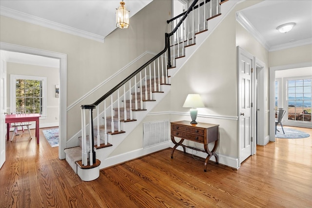 stairs featuring visible vents, wood finished floors, baseboards, and ornamental molding