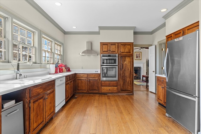 kitchen with light countertops, wall chimney exhaust hood, brown cabinets, and stainless steel appliances