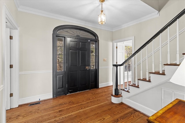 entryway featuring stairs, wood finished floors, visible vents, and ornamental molding