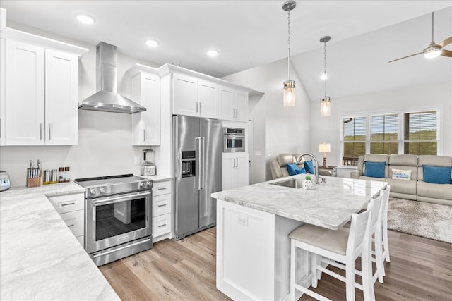 kitchen with sink, light stone counters, appliances with stainless steel finishes, wall chimney range hood, and white cabinets