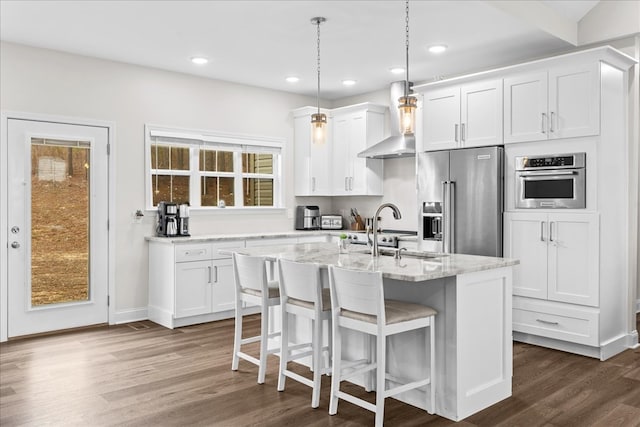 kitchen with white cabinets, stainless steel appliances, a kitchen island with sink, and wall chimney range hood