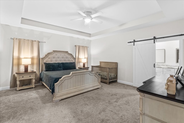 bedroom with connected bathroom, a raised ceiling, carpet floors, ceiling fan, and a barn door