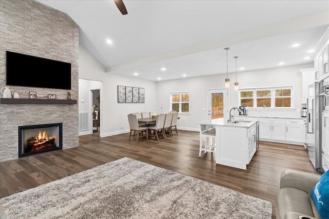 kitchen featuring pendant lighting, a fireplace, sink, white cabinets, and a kitchen island with sink