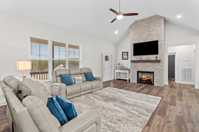 living room featuring hardwood / wood-style flooring, ceiling fan, a stone fireplace, and high vaulted ceiling