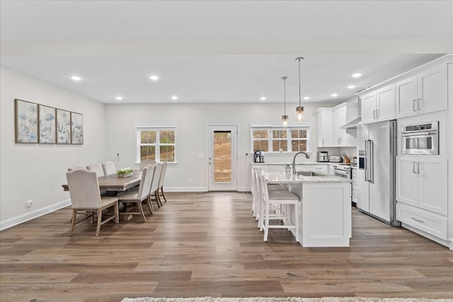 kitchen featuring appliances with stainless steel finishes, pendant lighting, an island with sink, white cabinets, and light stone countertops