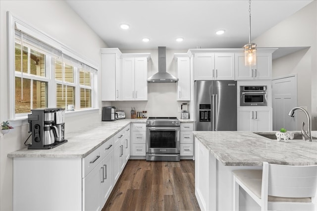 kitchen featuring sink, high end appliances, white cabinetry, pendant lighting, and wall chimney range hood