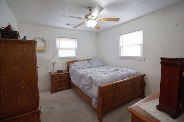 carpeted bedroom featuring multiple windows, visible vents, and ceiling fan