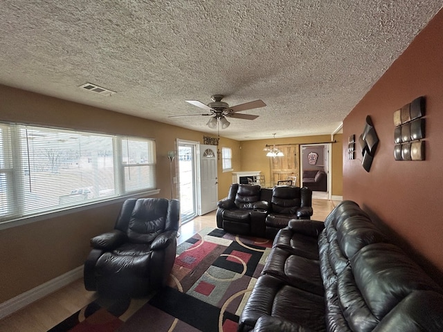 living area with visible vents, baseboards, a textured ceiling, and ceiling fan