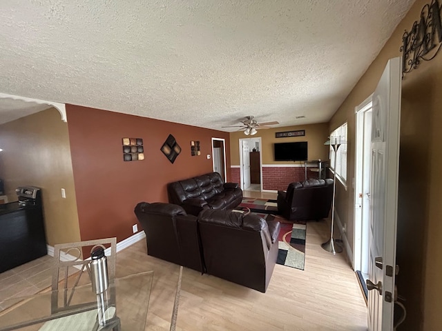 home theater featuring baseboards, light wood-style floors, a ceiling fan, and a textured ceiling