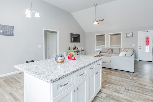 kitchen featuring a kitchen island, white cabinetry, hanging light fixtures, light stone countertops, and light hardwood / wood-style flooring