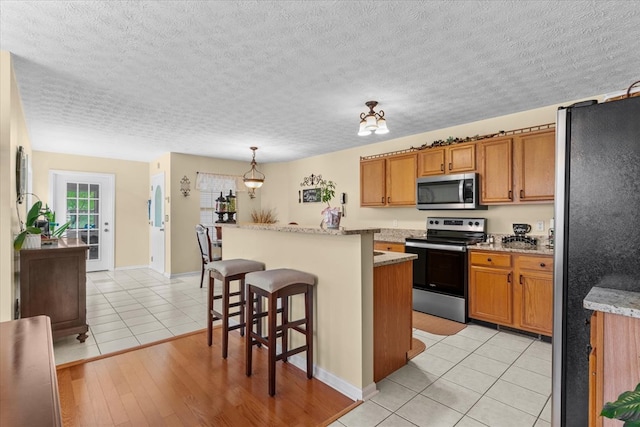 217 Valley Rd, Chatsworth, GA 30705 - kitchen featuring appliances with stainless steel finishes, brown cabinets, a center island, a breakfast bar, and light tile patterned flooring