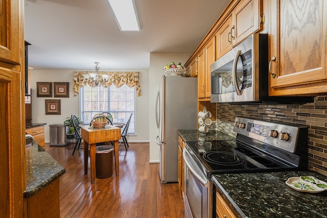 kitchen with appliances with stainless steel finishes, tasteful backsplash, hanging light fixtures, dark wood-type flooring, and an inviting chandelier