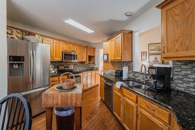 kitchen with sink, dark wood-type flooring, stainless steel appliances, a center island, and dark stone counters