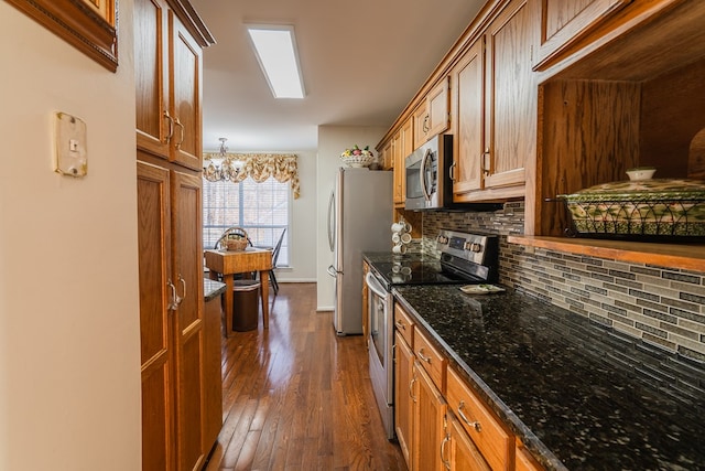 kitchen featuring appliances with stainless steel finishes, tasteful backsplash, dark stone counters, hanging light fixtures, and dark wood-type flooring