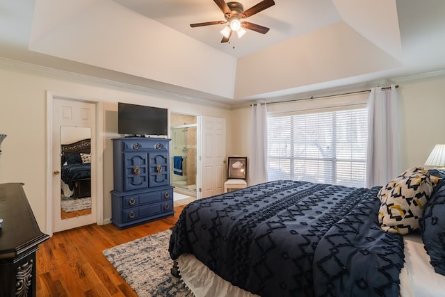 bedroom with connected bathroom, wood-type flooring, ornamental molding, and a raised ceiling