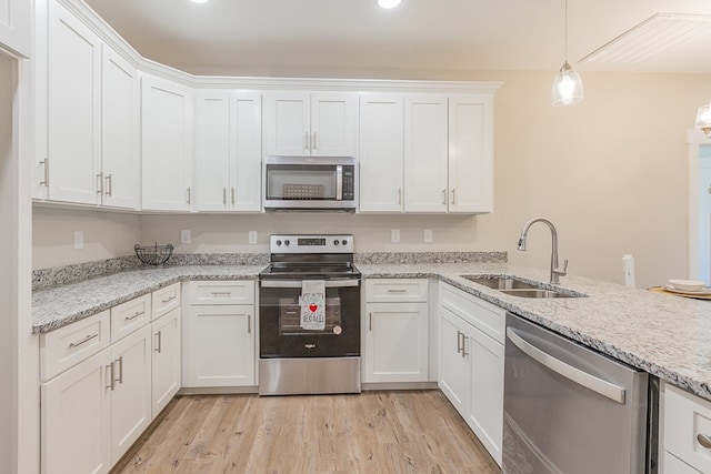 kitchen featuring decorative light fixtures, light wood-style flooring, white cabinets, stainless steel appliances, and a sink