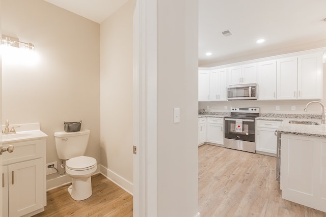 interior space with appliances with stainless steel finishes, white cabinetry, sink, light stone countertops, and light wood-type flooring