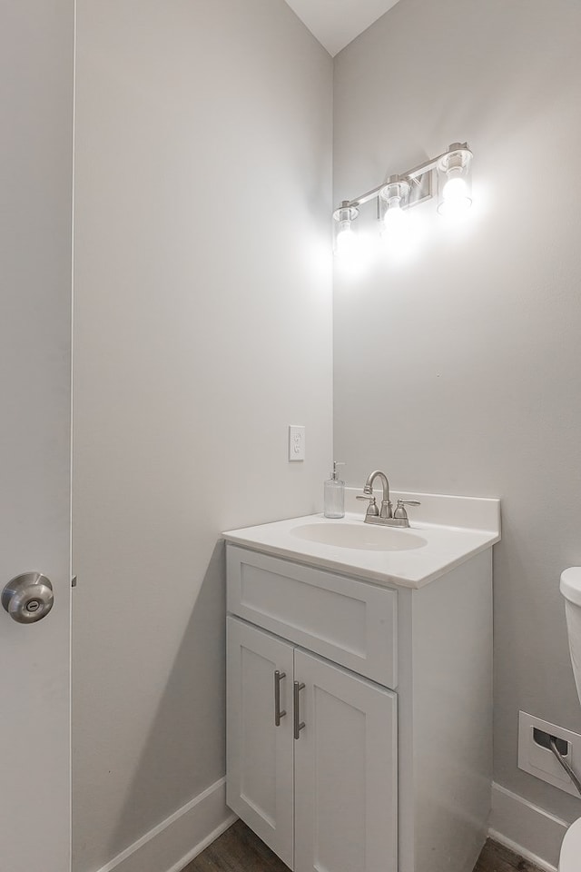half bath featuring baseboards, toilet, and vanity