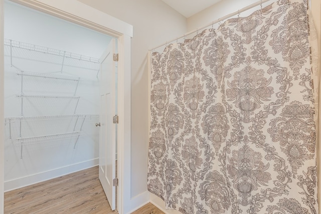 bathroom featuring curtained shower, a walk in closet, wood finished floors, and baseboards