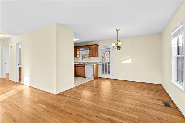 unfurnished living room featuring a healthy amount of sunlight, a notable chandelier, and light wood-type flooring