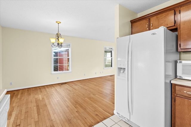 kitchen with pendant lighting, white appliances, light hardwood / wood-style floors, and a chandelier