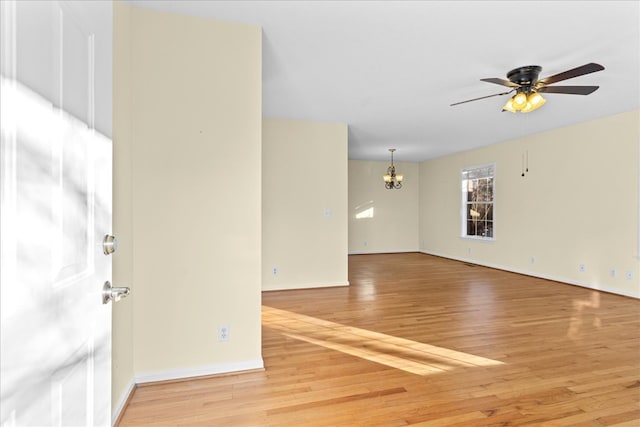 empty room featuring ceiling fan with notable chandelier and light hardwood / wood-style floors