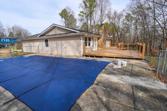 back of house featuring a deck, a covered pool, fence, and a chimney