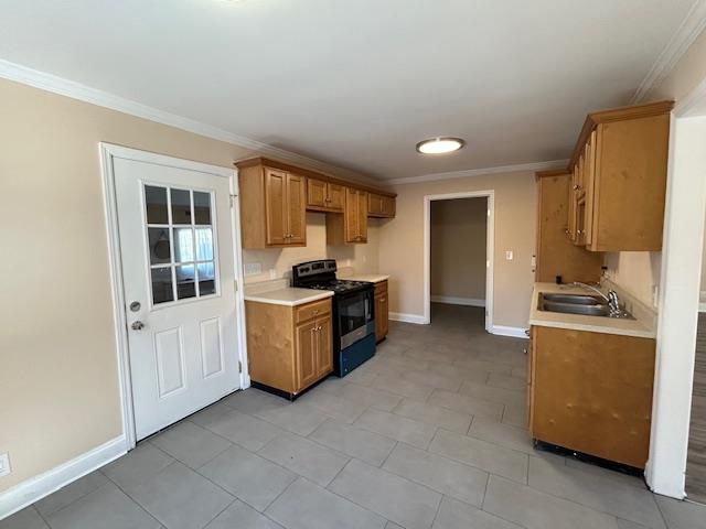 kitchen with black stove, baseboards, light countertops, ornamental molding, and a sink