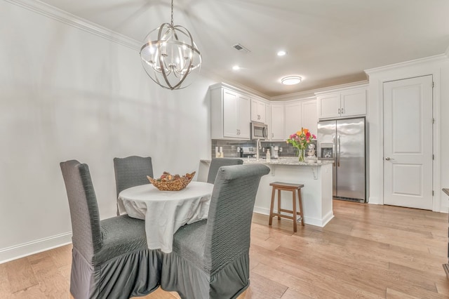 dining area featuring ornamental molding, an inviting chandelier, and light hardwood / wood-style floors