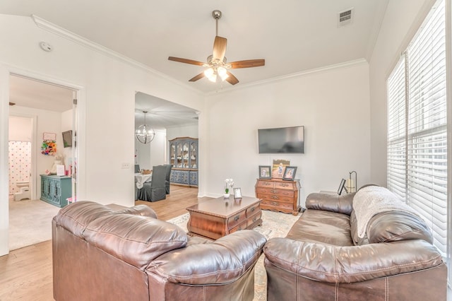 living room with ceiling fan with notable chandelier, ornamental molding, and light wood-type flooring