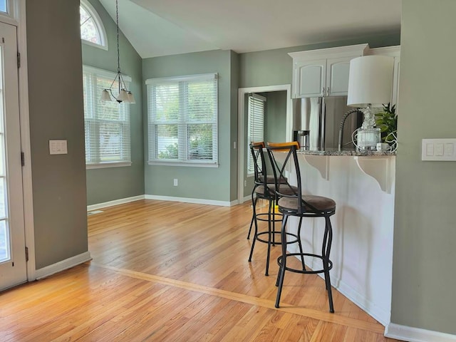 kitchen with stone countertops, a breakfast bar, white cabinetry, stainless steel refrigerator with ice dispenser, and light wood-type flooring