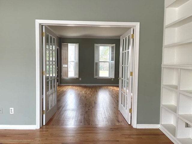 unfurnished room featuring hardwood / wood-style flooring, crown molding, built in shelves, and french doors