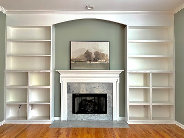 unfurnished living room featuring hardwood / wood-style flooring, a premium fireplace, crown molding, and built in shelves