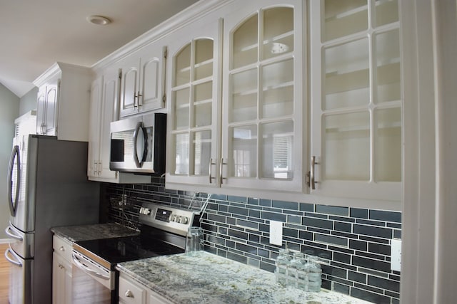 kitchen with white cabinetry, light stone counters, ornamental molding, stainless steel appliances, and decorative backsplash