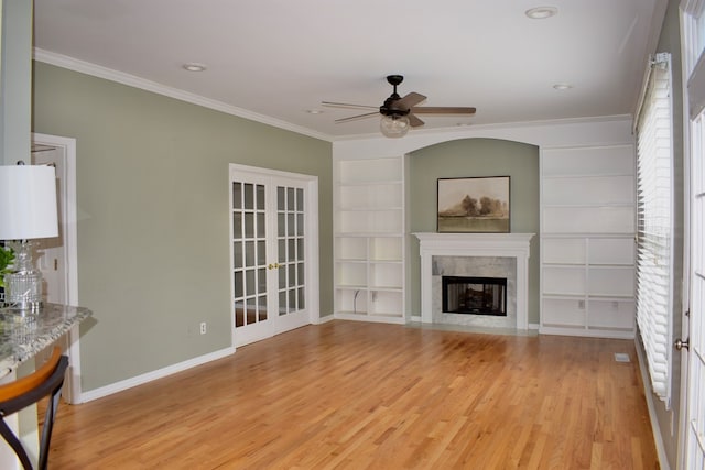 unfurnished living room featuring crown molding, built in shelves, light hardwood / wood-style floors, and french doors