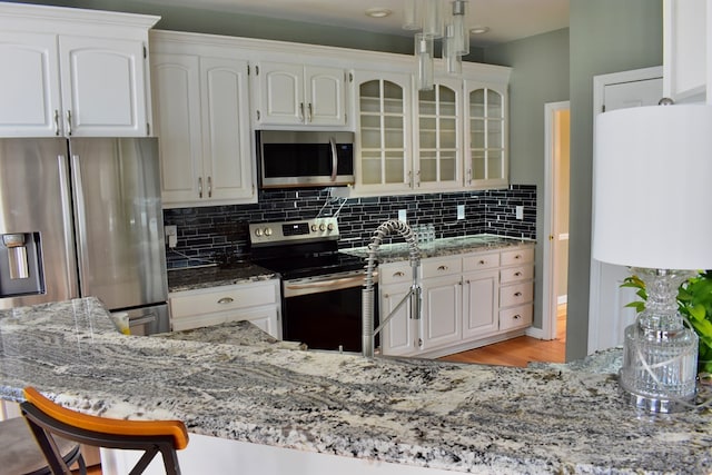 kitchen featuring light stone counters, decorative backsplash, white cabinets, and appliances with stainless steel finishes