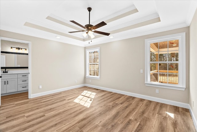 interior space with a tray ceiling, light wood-type flooring, crown molding, and a sink