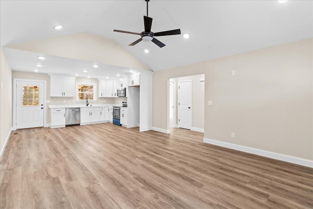 unfurnished living room featuring baseboards, lofted ceiling, a sink, and light wood-style flooring