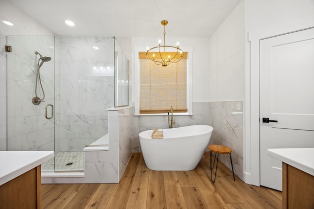 full bath with wood finished floors, a marble finish shower, an inviting chandelier, a freestanding tub, and tile walls