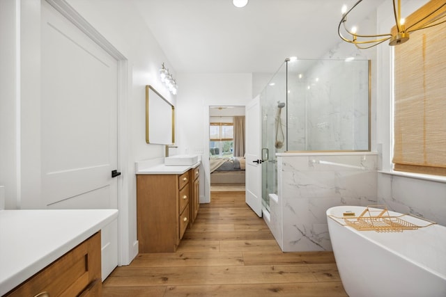 full bath featuring a freestanding tub, hardwood / wood-style flooring, a marble finish shower, an inviting chandelier, and vanity