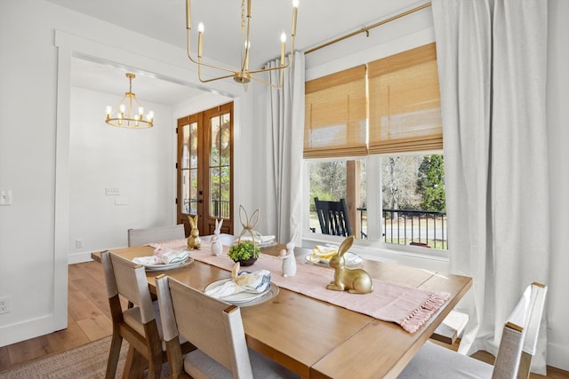 dining area featuring french doors, a notable chandelier, a healthy amount of sunlight, and wood finished floors