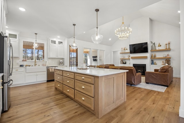 kitchen with light wood finished floors, a fireplace, appliances with stainless steel finishes, white cabinetry, and a center island