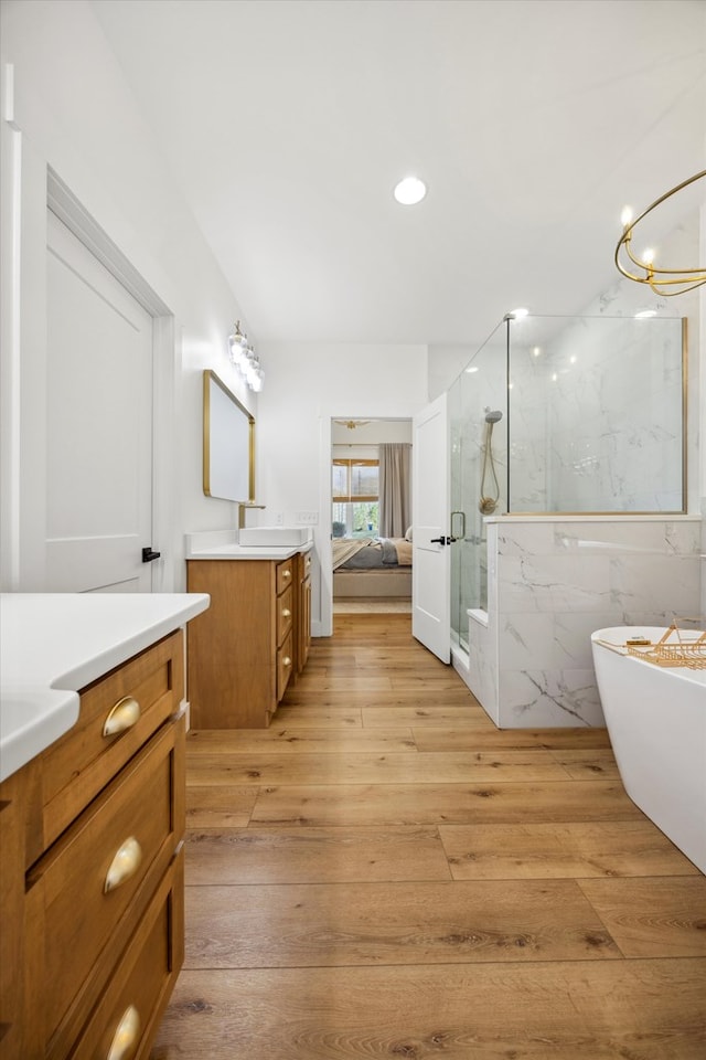 bathroom featuring a marble finish shower, two vanities, recessed lighting, a soaking tub, and wood-type flooring