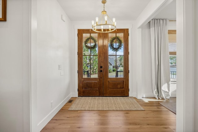 foyer entrance featuring an inviting chandelier, a wealth of natural light, baseboards, and light wood finished floors