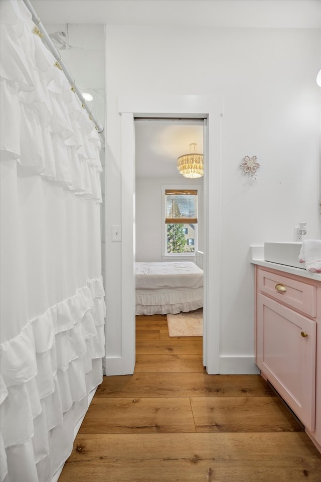bathroom with a shower with curtain, ensuite bathroom, wood finished floors, baseboards, and vanity