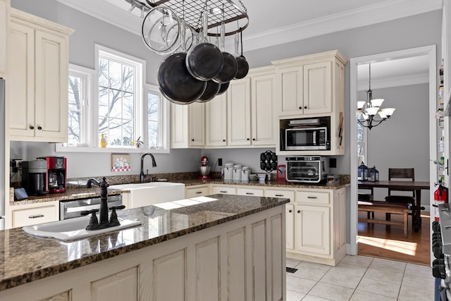 kitchen with a notable chandelier, crown molding, cream cabinets, and dark stone counters